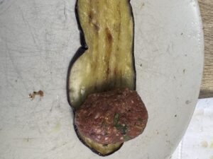קציצת בשר מונחת בקצה פרוסת חציל לפני הגלגול